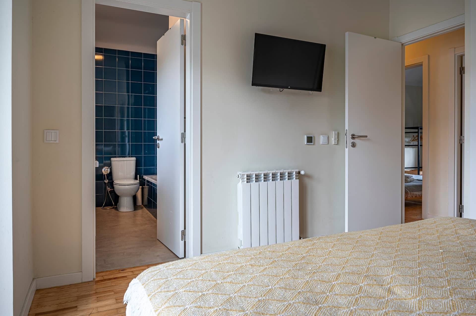 A bedroom with a bed, a television mounted on the wall, and a bathroom visible through an open door.