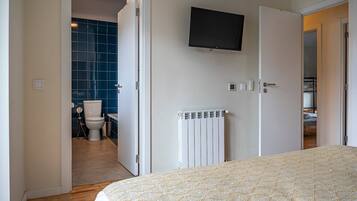 A bedroom with a bed, a television mounted on the wall, and a bathroom visible through an open door.