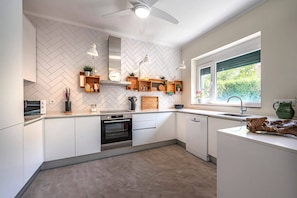 A modern kitchen with white cabinetry, a herringbone-patterned backsplash, built-in appliances, and a window with a view of greenery.