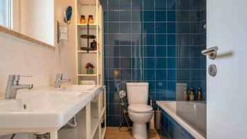 A bathroom with a white sink, a toilet, and a bathtub. There is a shelf with toiletries and a potted plant.