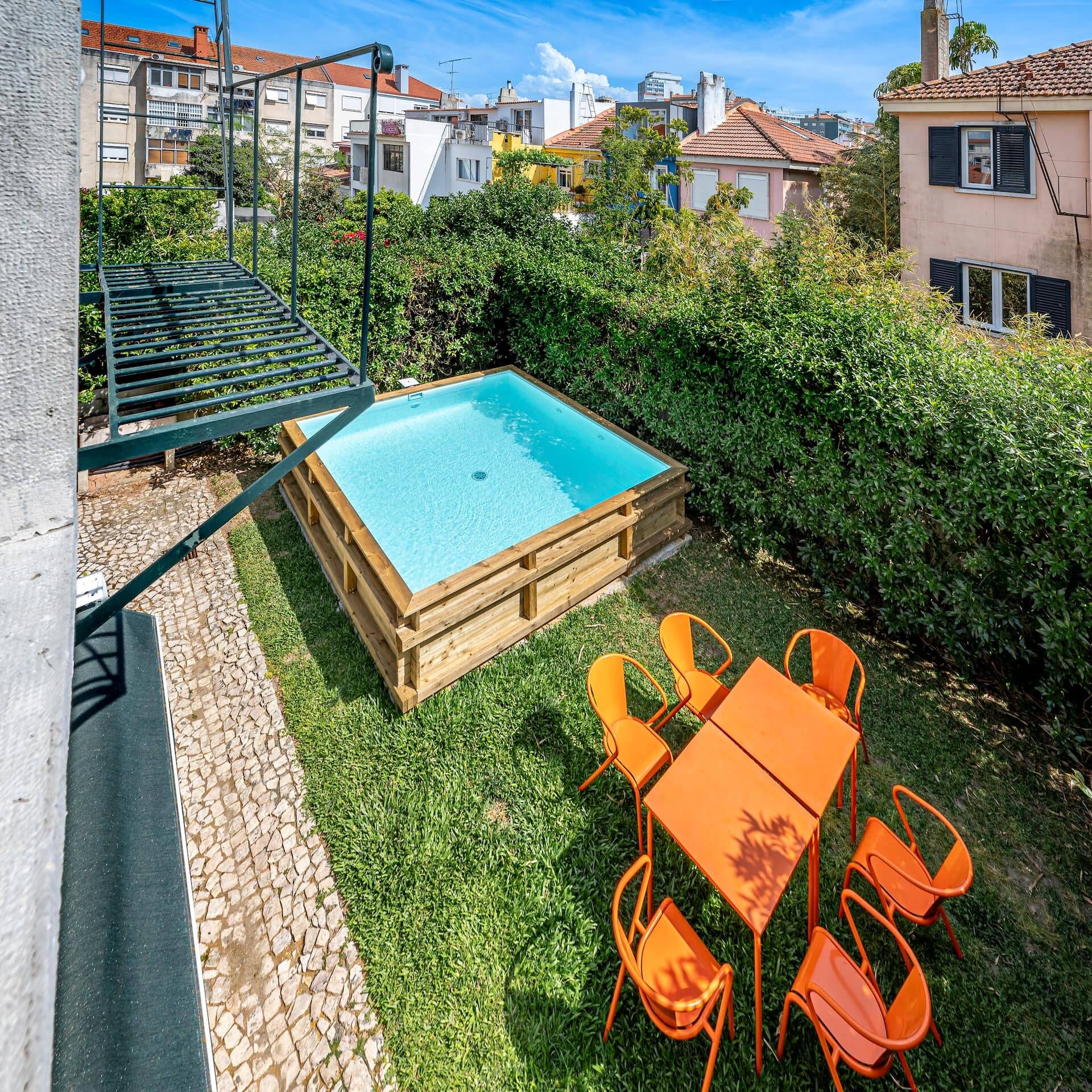 A rectangular pool with a wooden deck, surrounded by a grassy area and orange chairs.