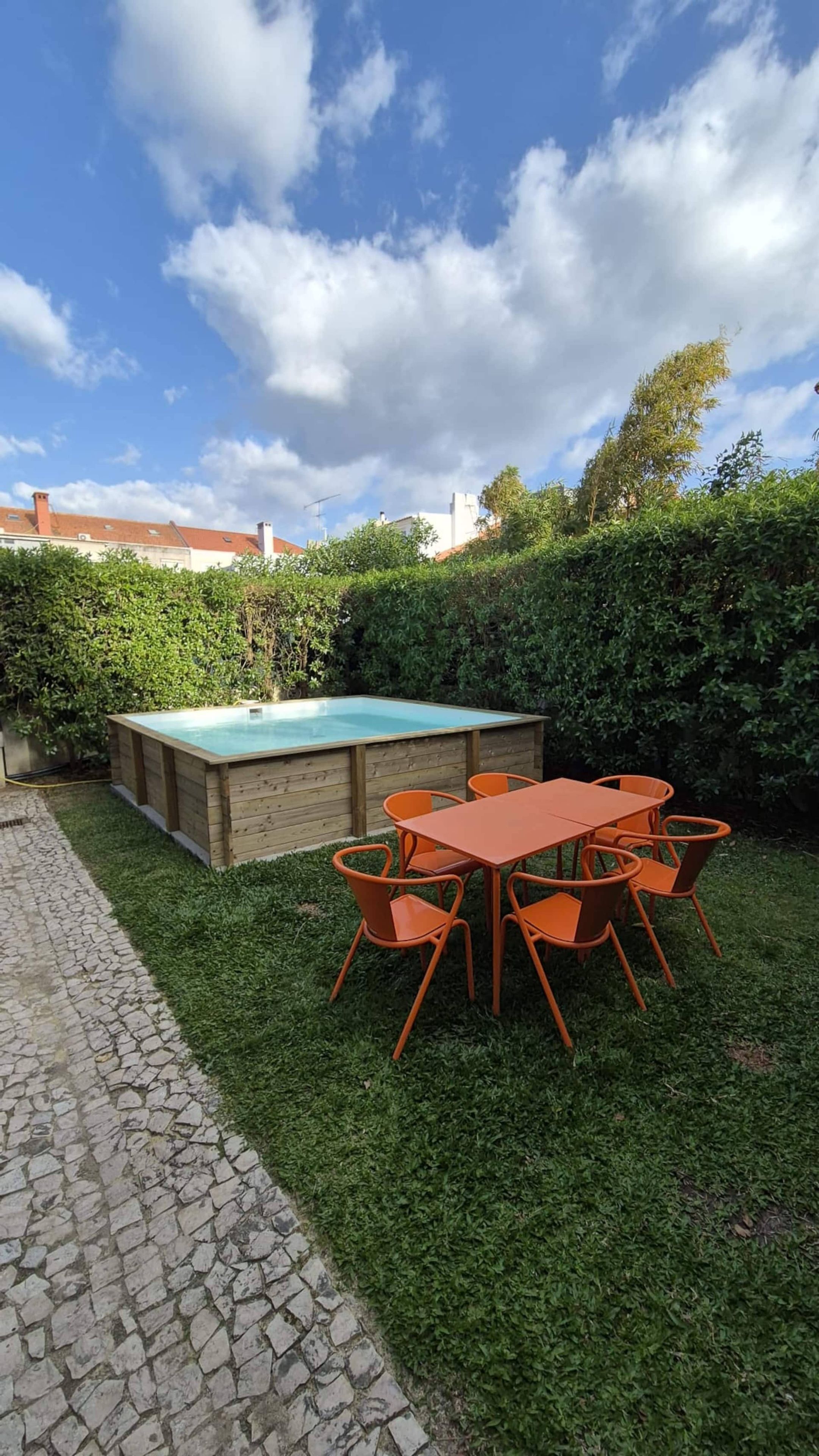 A backyard with a swimming pool, a table with chairs, and a hedge.