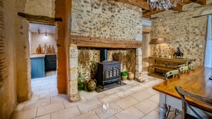 Un intérieur rustique avec des murs en pierre apparentes, un plafond en bois, une cheminée en pierre et un coin repas comprenant une table et des chaises en bois.