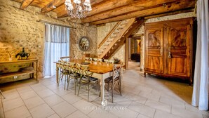 Une salle à manger rustique avec une table et des chaises en bois, un lustre et un escalier menant à une autre pièce.