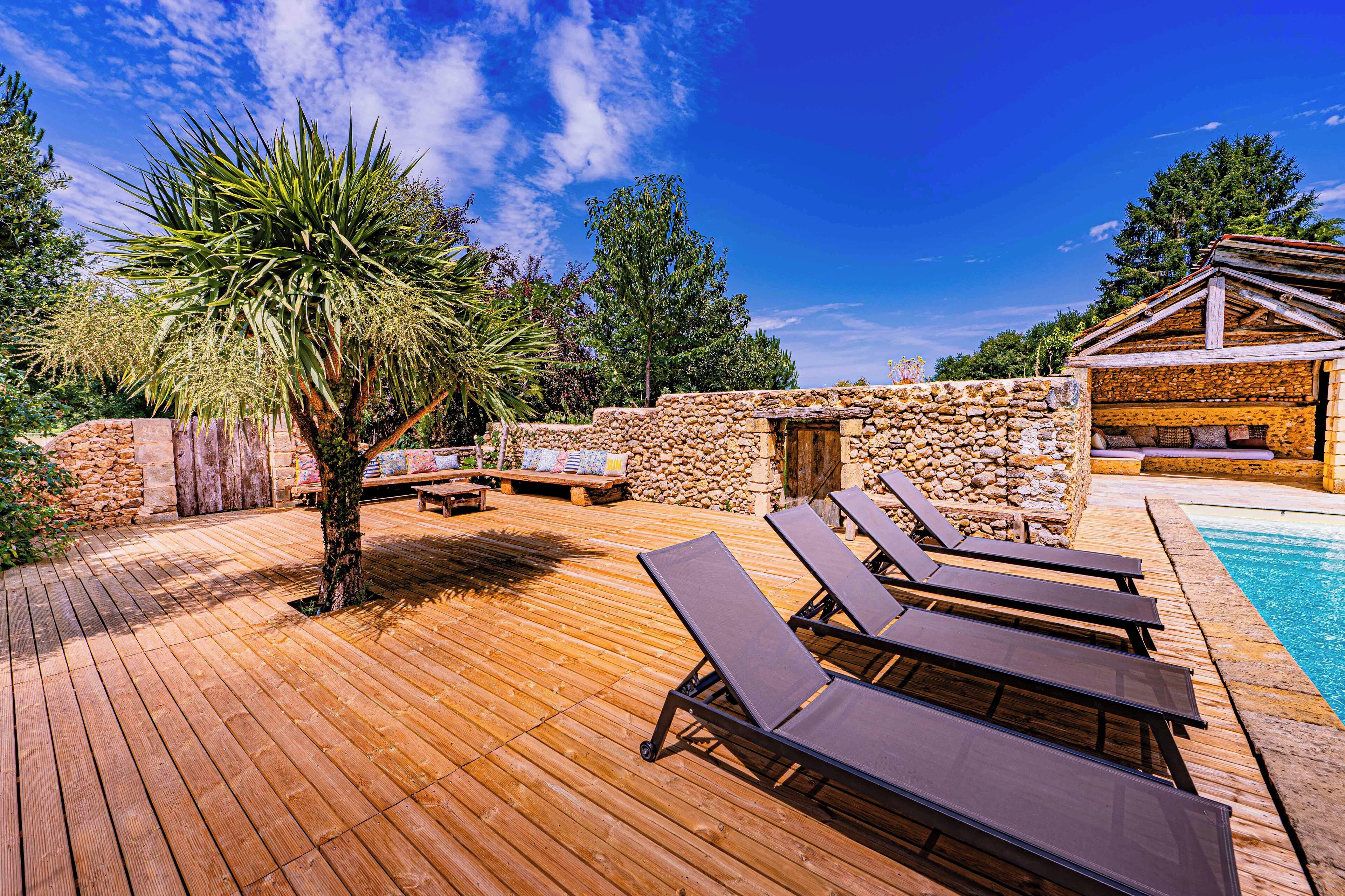 A wooden deck with lounge chairs, a stone wall, and a pool.