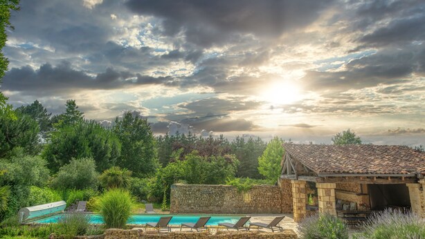 Un espace piscine avec des chaises longues, un bâtiment en pierre et une végétation luxuriante.