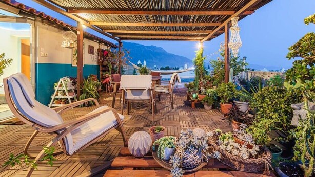 Eine Terrasse im Freien mit Holzmöbeln, Kübelpflanzen und Blick auf das Meer.