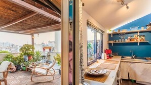 Eine kompakte Küche mit Blick auf die Stadt, ein Essbereich mit Tisch und Stühlen sowie ein Balkon mit Holzboden und einem Stuhl.