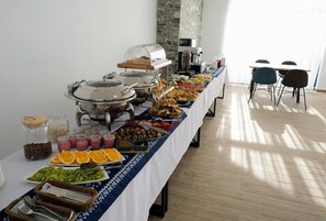 A buffet table with various food items, including fruits, pastries, and beverages, set up in a room with a stone wall and a table with chairs. - Hotel Posta Mestia (Mestia)