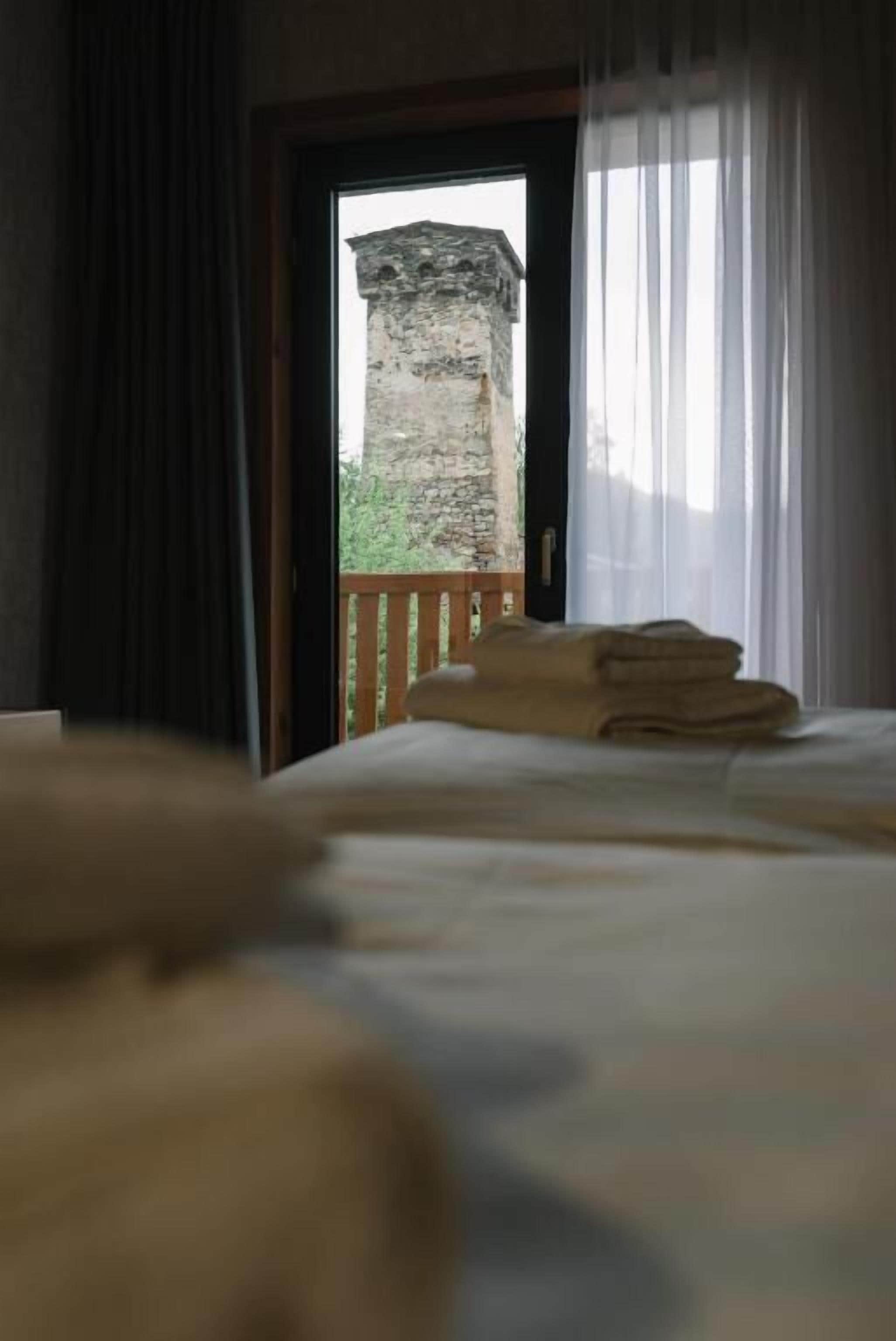 Quarto de hotel com uma cama, uma janela com cortinas e vista para uma construção de pedra lá fora.