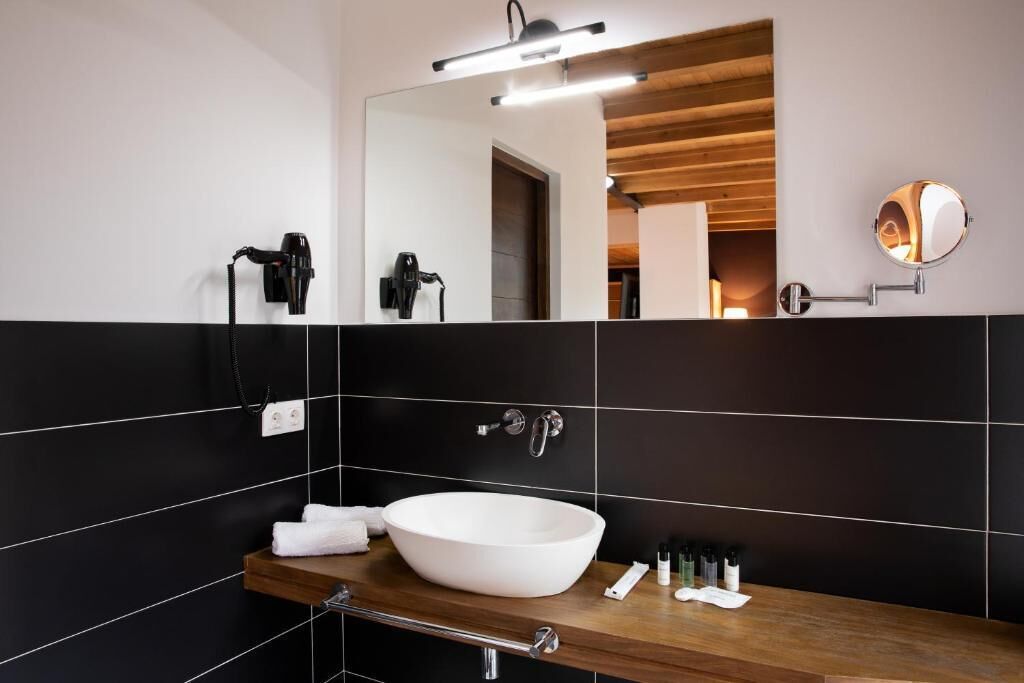 Un bagno moderno con un grande specchio, piastrelle bianche e nere, un mobile contenitore in legno e un lavandino bianco.