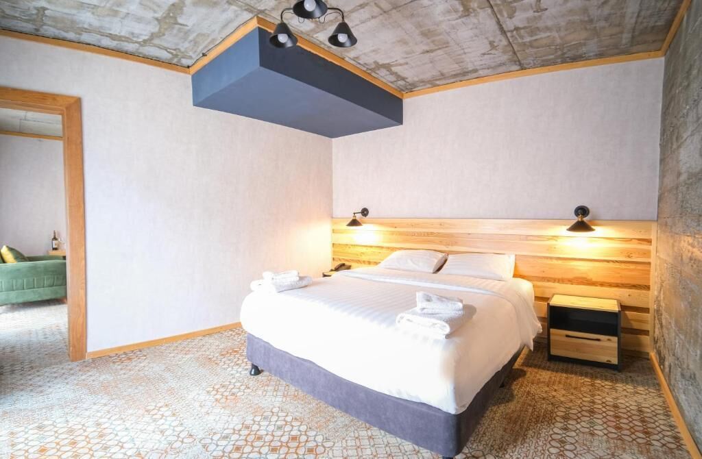 A modern hotel room with a large bed, two bedside tables, a wooden headboard, and a ceiling light fixture.