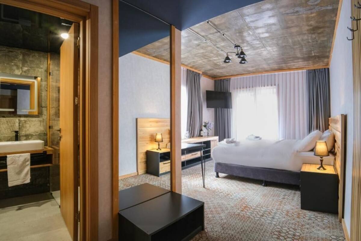 A modern hotel room with a large bed, bedside lamps, a TV, and a wooden-framed mirror.