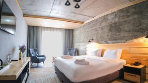 Una habitación de hotel moderna con una cama grande, un escritorio con silla, un televisor y un cabecero de madera.