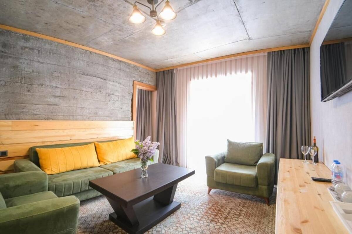 A hotel room with a green sofa, a green armchair, a wooden coffee table, and a TV mounted on the wall.