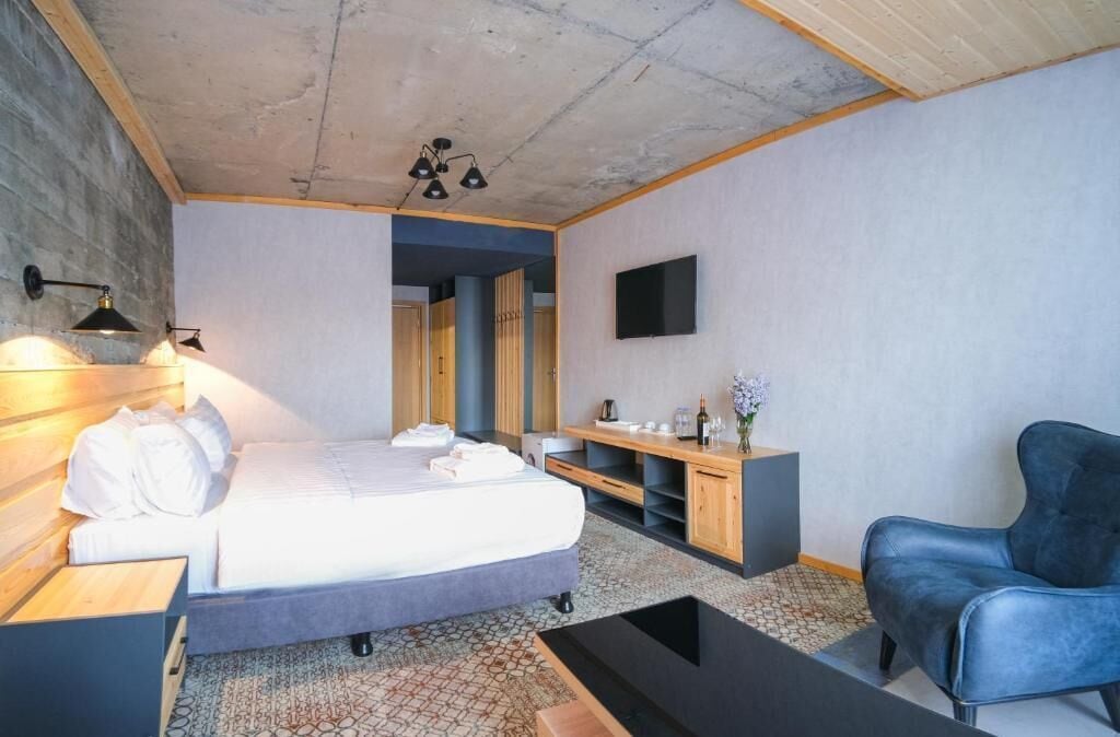 A modern bedroom with a bed, bedside table, lamp, TV, and a blue chair.