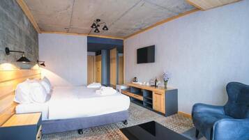 A modern bedroom with a bed, bedside table, lamp, TV, and a blue chair.