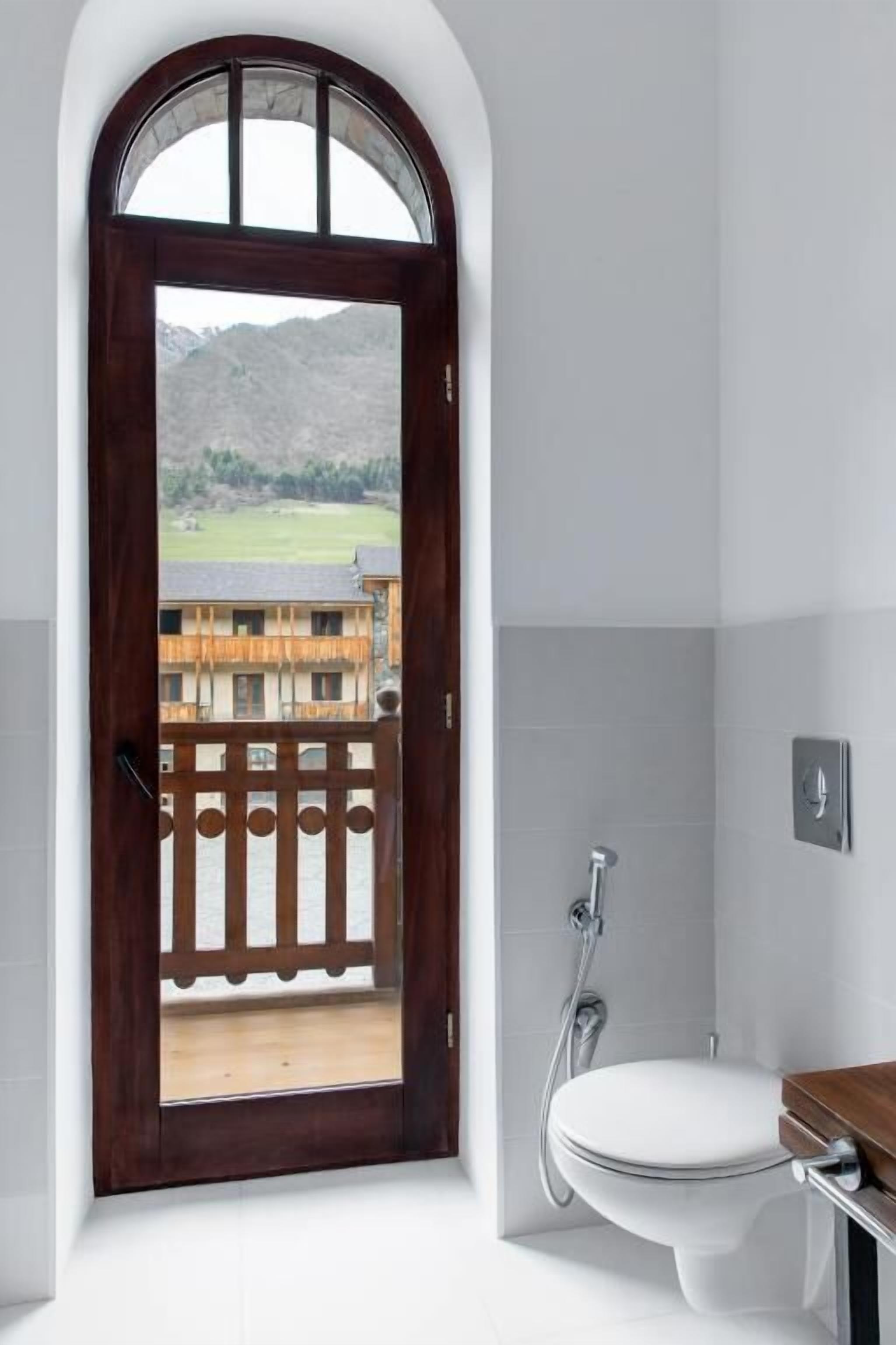 A bathroom with a wooden door leading to a balcony, a white toilet, and a shower.