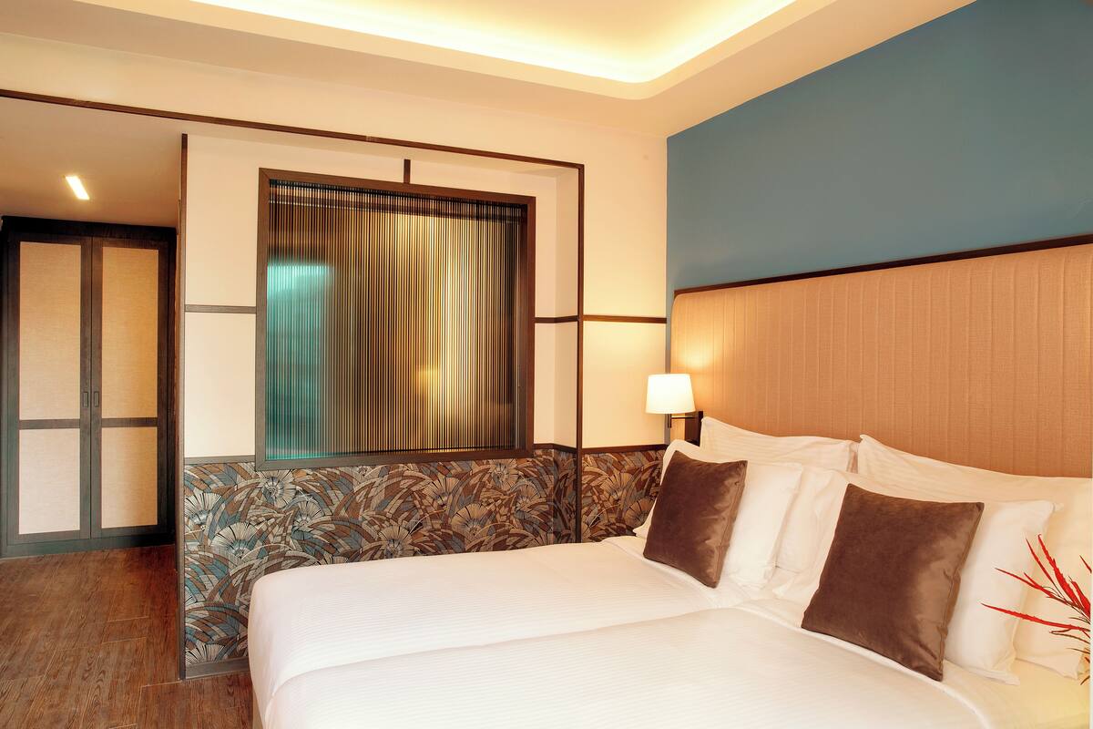 Ein Hotelzimmer mit einem großen Bett, einem Fenster mit Vorhängen, einer Wandlampe und einem Holzboden.
