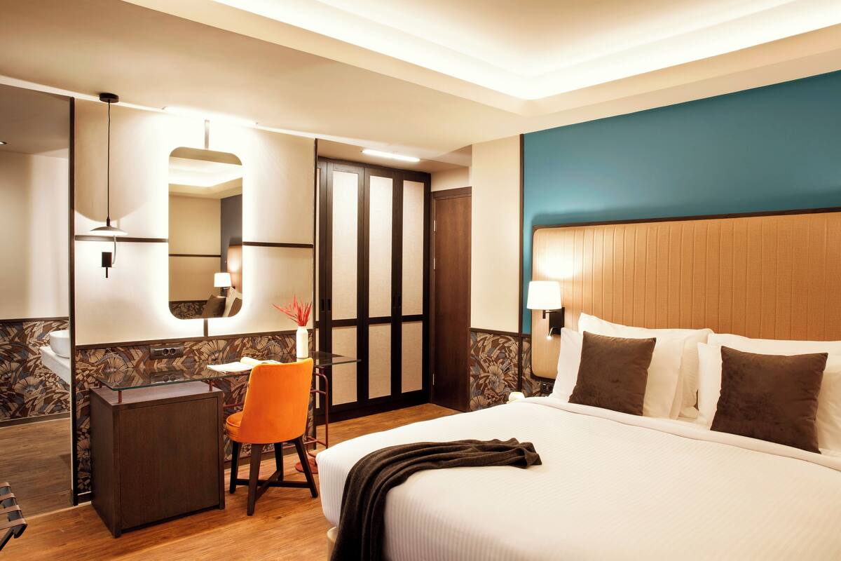 Ein Hotelzimmer mit Bett, Schreibtisch, Stuhl, Spiegel und Tür.