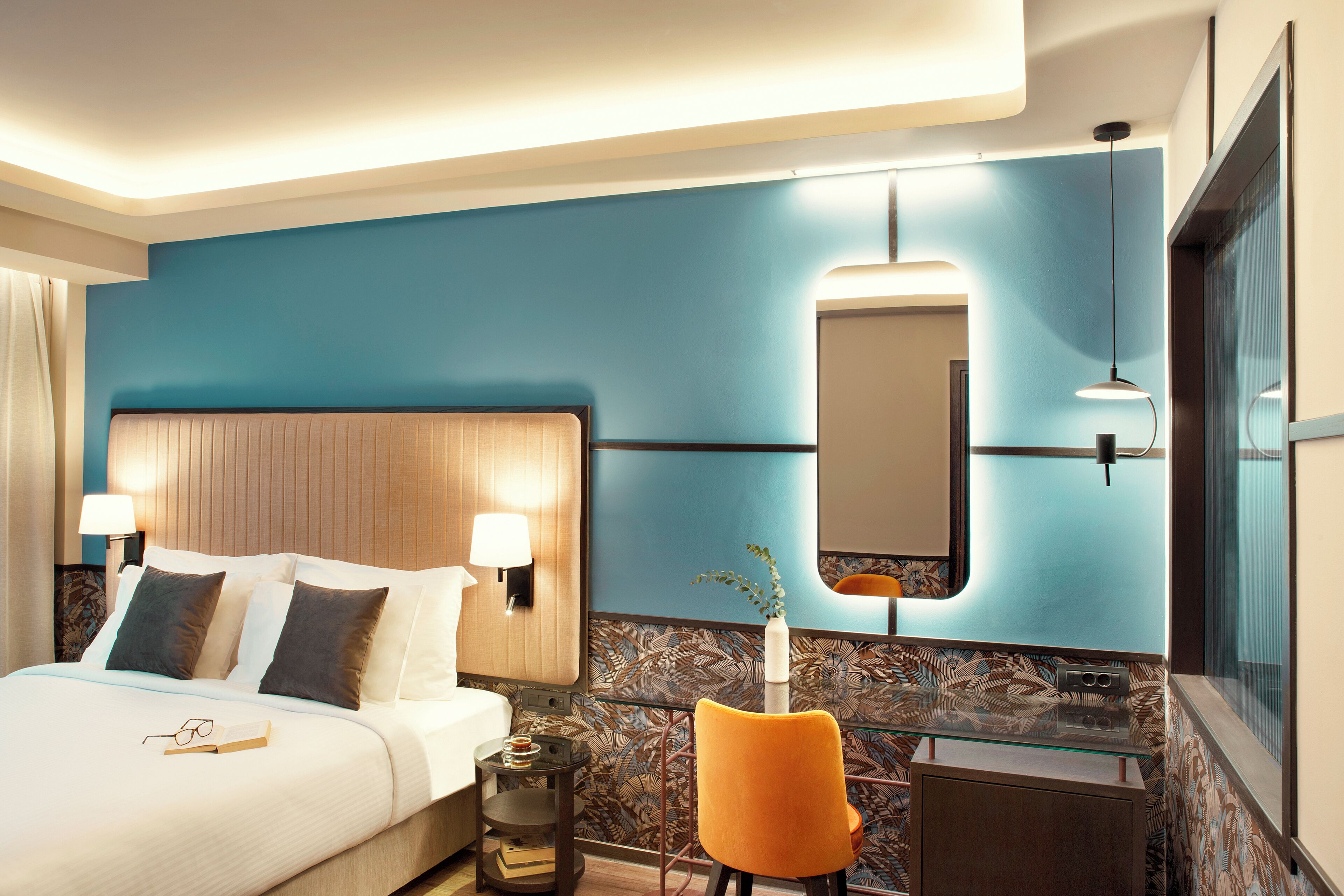 Une chambre d’hôtel avec un lit, des lampes de chevet, un miroir, une chaise et une petite table.