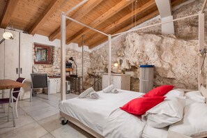 Une chambre avec un plafond en bois, des murs en pierre, un lit avec une literie blanche et des oreillers rouges, un bureau avec une chaise et une petite fenêtre.
