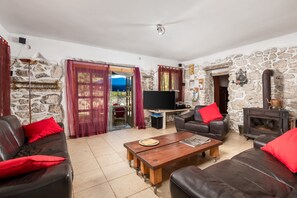 Un salon avec des murs en pierre, une cheminée, des canapés en cuir et un téléviseur.