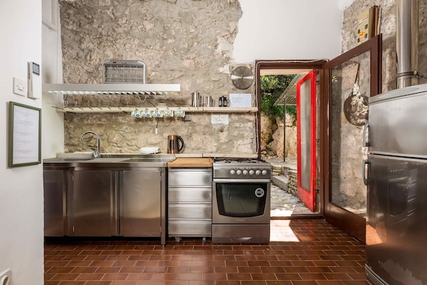 A compact kitchen with stainless steel appliances, a built-in oven, and a red-framed door leading outside. - Holiday House Cave Romana (Pula)