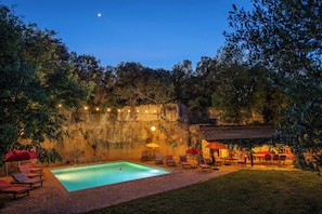 A swimming pool with lounge chairs and umbrellas, surrounded by trees and a stone wall.