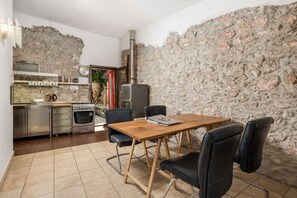 Une cuisine compacte avec un mur en pierre, une table en bois avec des chaises, un poêle et un réfrigérateur.