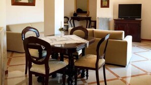 A dining area with a round table, chairs, a sofa, a television, and a mirror.