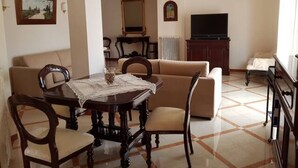 A dining area with a table and chairs, a sofa, a television, and a cabinet.