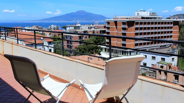A balcony with two white chairs and a view of a cityscape, including a mountain in the distance.