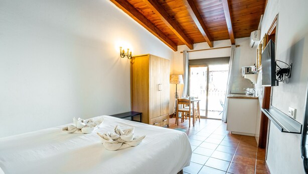 A hotel room with a bed, a desk, a chair, a kitchenette, and a bathroom visible through an open door. - Marbella Village  | Studio with Terrace (Marbella)