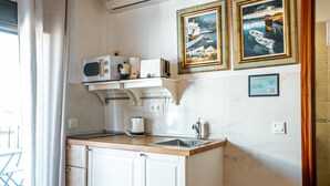 A compact kitchen with white cabinets, a wooden countertop, a microwave, a toaster, and a sink. There are two framed paintings on the wall and a QR code below them. - Marbella Village  | Studio with Terrace (Marbella)