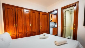 A hotel room with a large bed, wooden wardrobe, and a bathroom with a glass shower.