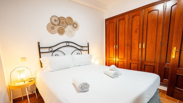 A neatly made bed with white linens and two rolled towels, a bedside lamp, and a wall-mounted decorative item.
