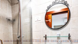 A bathroom with a glass-enclosed shower, a white pedestal sink, and a round mirror with a decorative frame. - Marbella Village  | Budget Ground Floor Unit (Marbella)