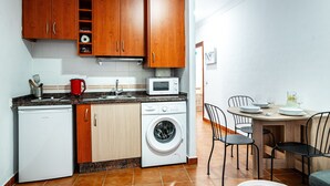 A compact kitchen with wooden cabinets, a washing machine, a microwave, and a dining area with a table and chairs. - Marbella Village  | Budget Ground Floor Unit (Marbella)