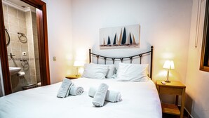 A neatly made bed with rolled towels, a painting above the bed, and two bedside lamps. - Marbella Village  | Budget Ground Floor Unit (Marbella)