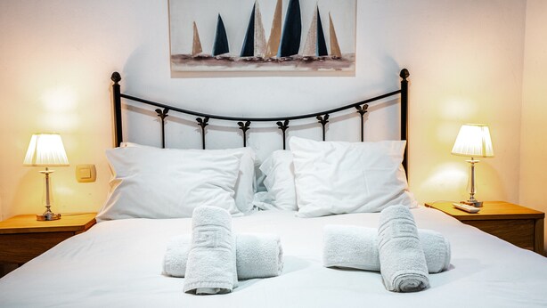 A neatly made bed with white linens and towels arranged in a heart shape, flanked by two bedside lamps and a painting of sailboats on the wall. - Marbella Village  | Budget Ground Floor Unit (Marbella)