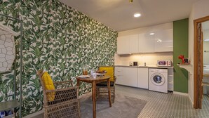 Een kleine keuken met een wasmachine, een eettafel met stoelen en behang met een patroon.