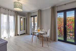 A spacious dining area with a table set for two, a modern chandelier, and a view of a garden through a sliding glass door. - Ancha Village | Boho Suite (Marbella)