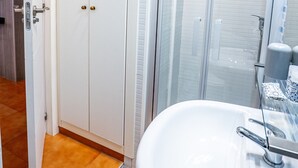 Kylpyhuoneessa on valkoinen pesuallas, lasinen suihkuseinä ja valkoinen vaatekaappi, jossa on ovi.