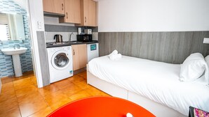 Pieni hotellihuone, jossa on sänky, pesukone, pesuallas ja mikroaaltouuni.