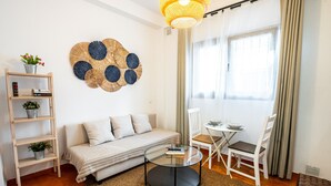 Ein modernes Wohnzimmer mit einer Couch, einem Glastisch, einem Bücherregal und einem Essbereich mit Tisch und Stühlen.