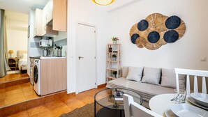 Ein kompakter Wohnraum mit einer Küchenzeile, einem Sofa, einem Glastisch und einem Wanddekor.