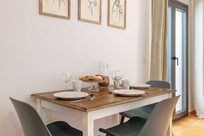 A dining table with plates, glasses, and a pitcher, set against a white wall with framed botanical prints.