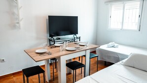 A hotel room with a bed, a desk with a chair, a television, and a window. - Escuela Village | Budget Quadruple Apartment (Marbella)