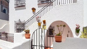 A white building with a staircase, potted plants, and a gated entrance.
